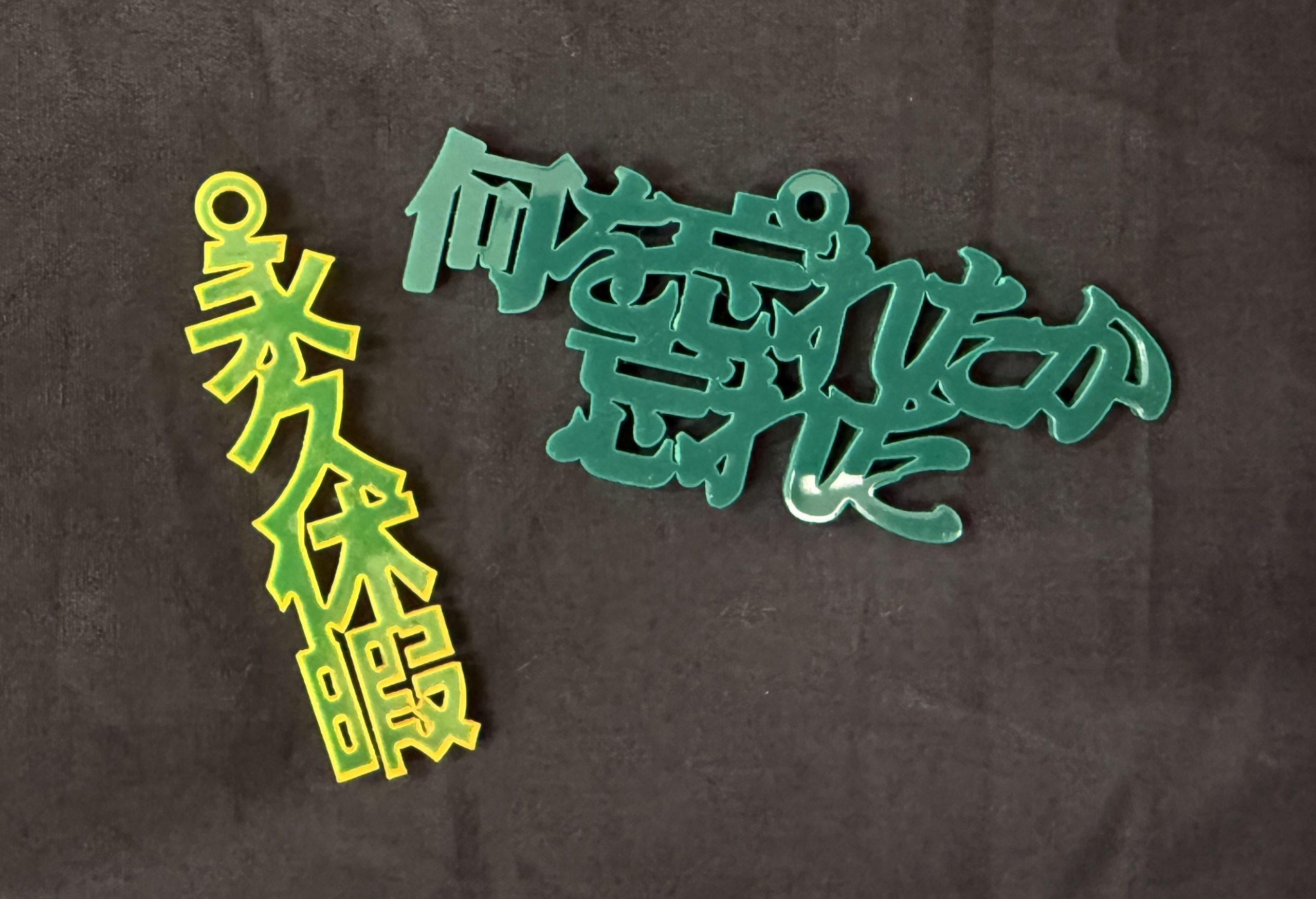 左 黄色いアクリルで永久休暇とカットされたキーホルダー 右 緑のアクリルで何を忘れたか忘れたとカットされたキーホルダー